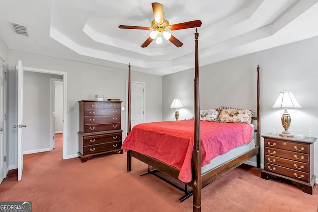 carpeted bedroom with a tray ceiling, a ceiling fan, visible vents, and baseboards