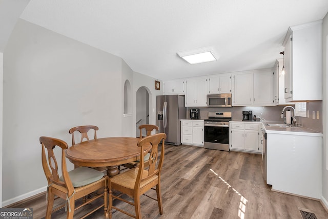 kitchen with white cabinets, appliances with stainless steel finishes, wood finished floors, light countertops, and a sink