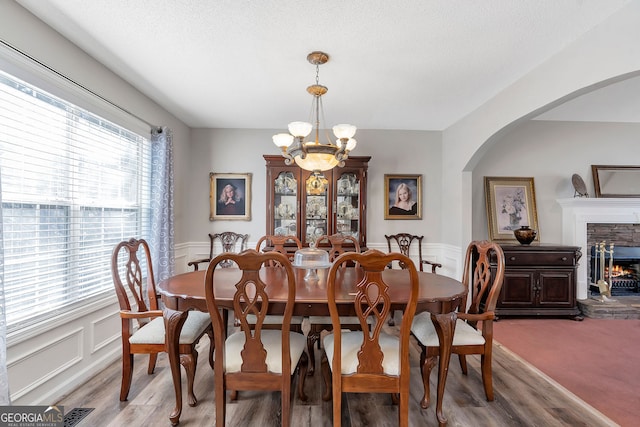 dining area with a fireplace, a decorative wall, wainscoting, wood finished floors, and a chandelier