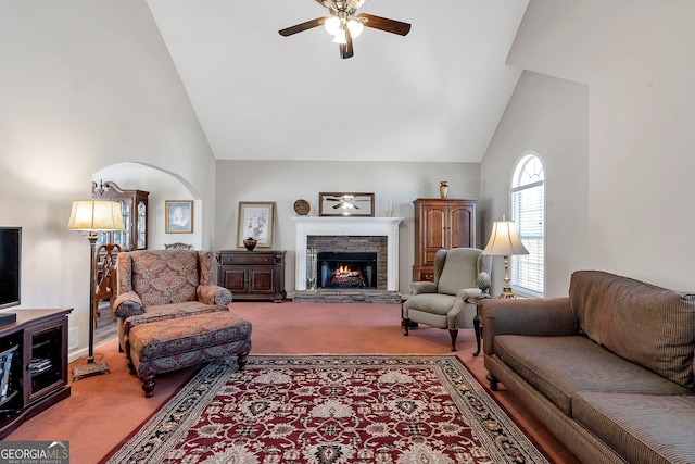 carpeted living area with high vaulted ceiling, ceiling fan, and a stone fireplace