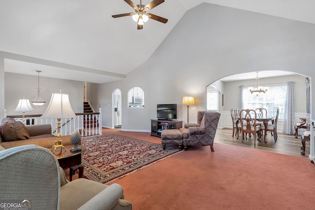 carpeted living area with arched walkways, high vaulted ceiling, ceiling fan with notable chandelier, and stairs