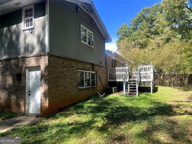 view of home's exterior with a yard, brick siding, a wooden deck, and central air condition unit