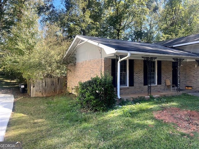 view of home's exterior with brick siding, a lawn, a porch, and fence