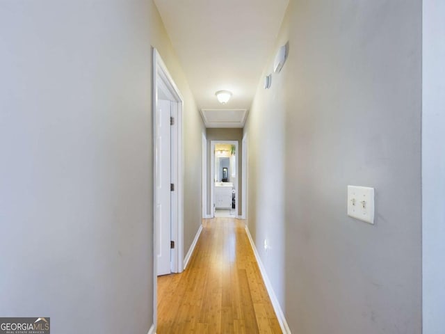 hall featuring attic access, light wood-style flooring, and baseboards