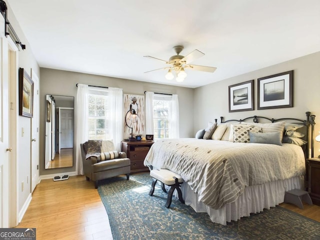 bedroom with light wood-style floors, a barn door, baseboards, and ceiling fan