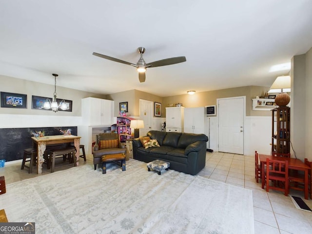 living room with light tile patterned floors, a wainscoted wall, and ceiling fan with notable chandelier