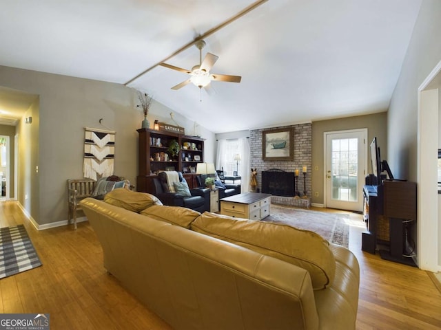 living room featuring baseboards, light wood-style floors, ceiling fan, vaulted ceiling, and a brick fireplace