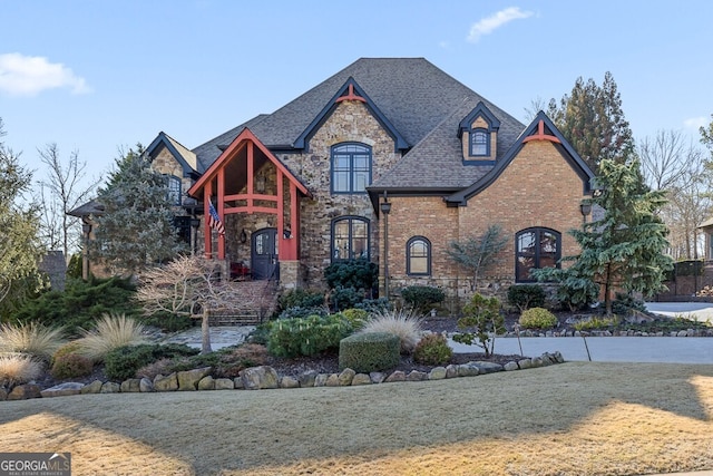 view of front facade featuring brick siding, stone siding, roof with shingles, french doors, and a front yard