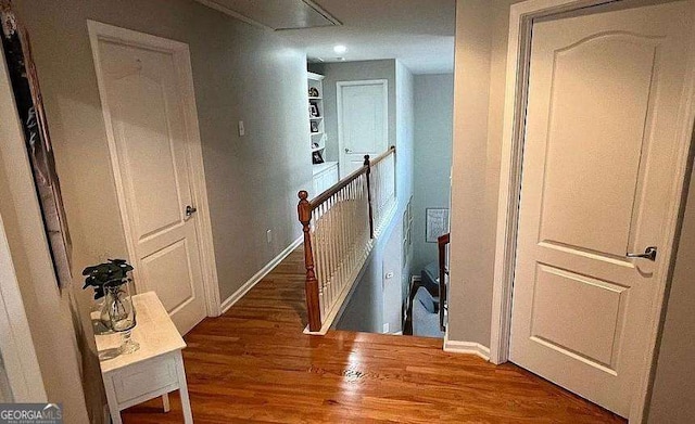 hallway with baseboards, wood finished floors, an upstairs landing, and attic access