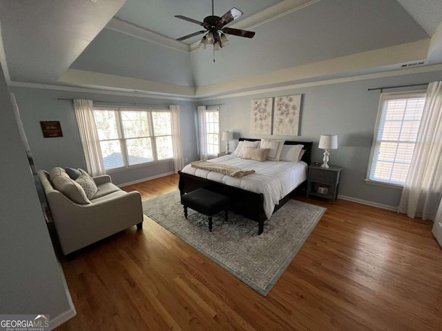 bedroom featuring ornamental molding, a tray ceiling, wood finished floors, and baseboards