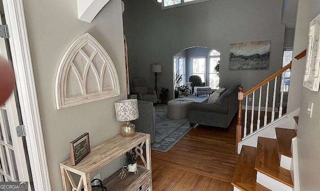 living room with arched walkways, a high ceiling, stairway, and wood finished floors