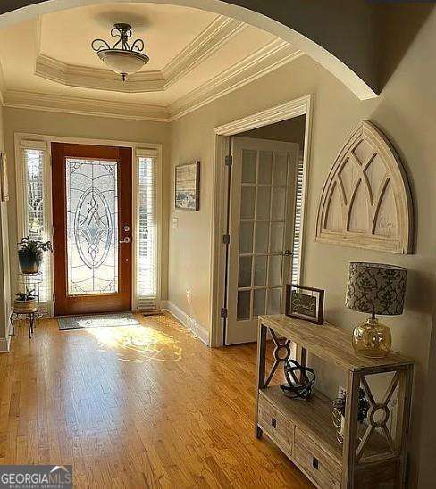 entrance foyer with arched walkways, ornamental molding, light wood-style flooring, and baseboards