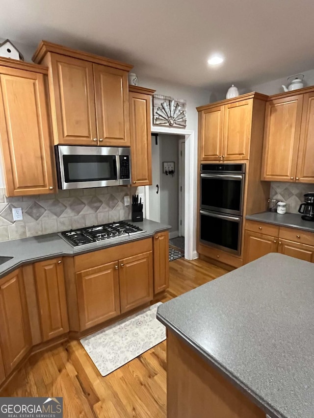 kitchen featuring light wood finished floors, tasteful backsplash, dark countertops, recessed lighting, and appliances with stainless steel finishes