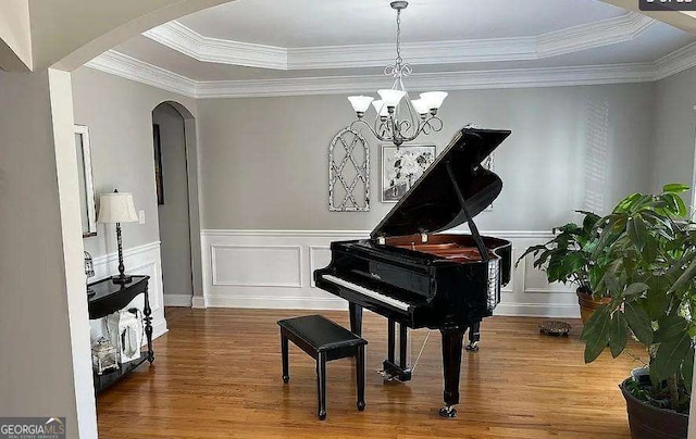 living area featuring arched walkways, a decorative wall, a wainscoted wall, wood finished floors, and a raised ceiling