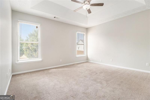 carpeted empty room featuring baseboards, visible vents, a tray ceiling, and a ceiling fan