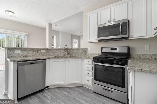 kitchen with light stone counters, stainless steel appliances, white cabinetry, a sink, and a textured ceiling