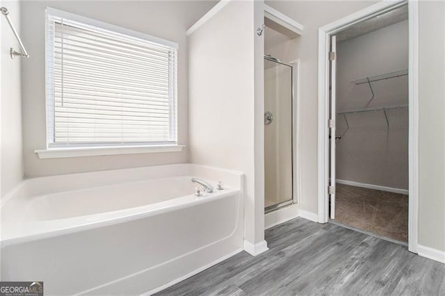 full bath with a garden tub, wood finished floors, baseboards, a spacious closet, and a stall shower