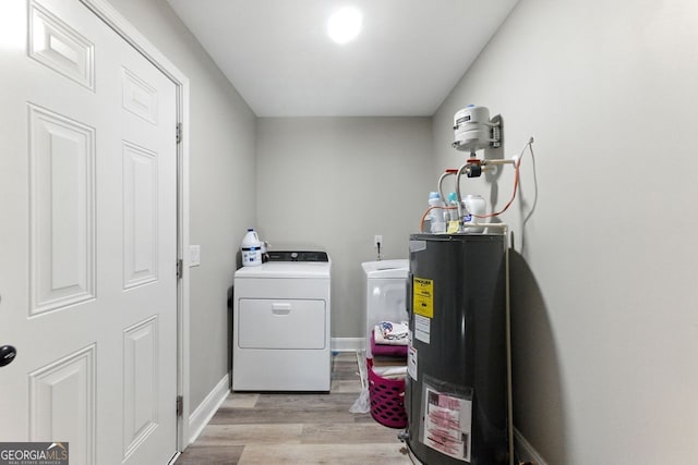 clothes washing area featuring light wood finished floors, water heater, washing machine and dryer, laundry area, and baseboards