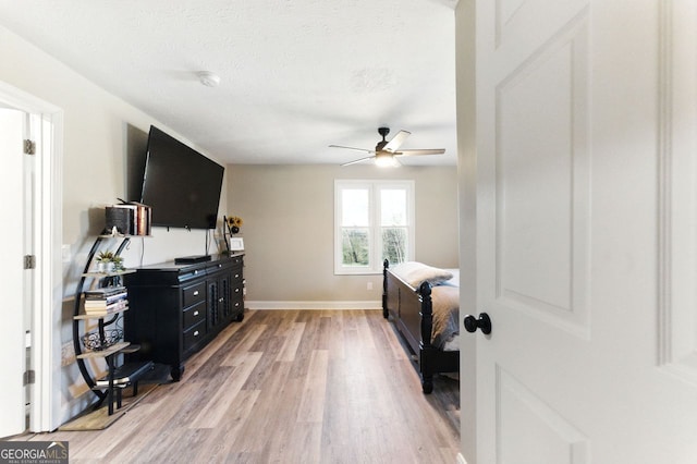 bedroom featuring light wood finished floors, a ceiling fan, baseboards, and a textured ceiling