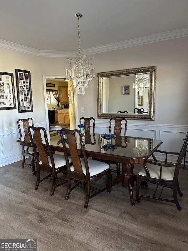 dining area with a wainscoted wall, ornamental molding, wood finished floors, a chandelier, and a decorative wall