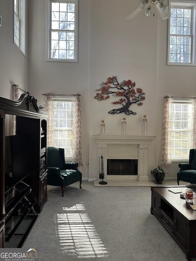 carpeted living room featuring a ceiling fan, a fireplace with raised hearth, and a towering ceiling