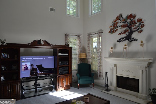 carpeted living area featuring a high ceiling, a fireplace, visible vents, and a healthy amount of sunlight