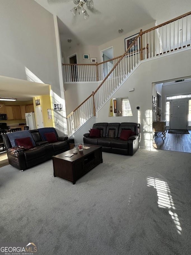 carpeted living room featuring ceiling fan, a high ceiling, stairway, and visible vents