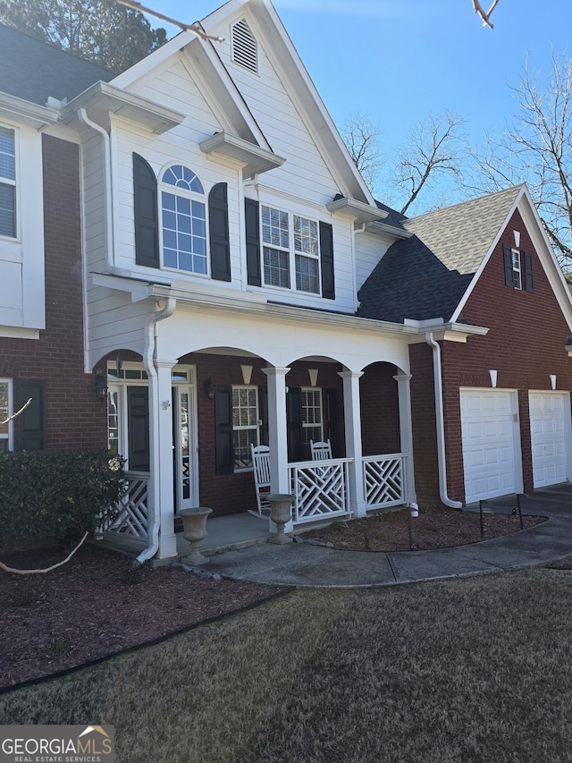 view of front of home featuring a porch, a garage, a shingled roof, brick siding, and driveway