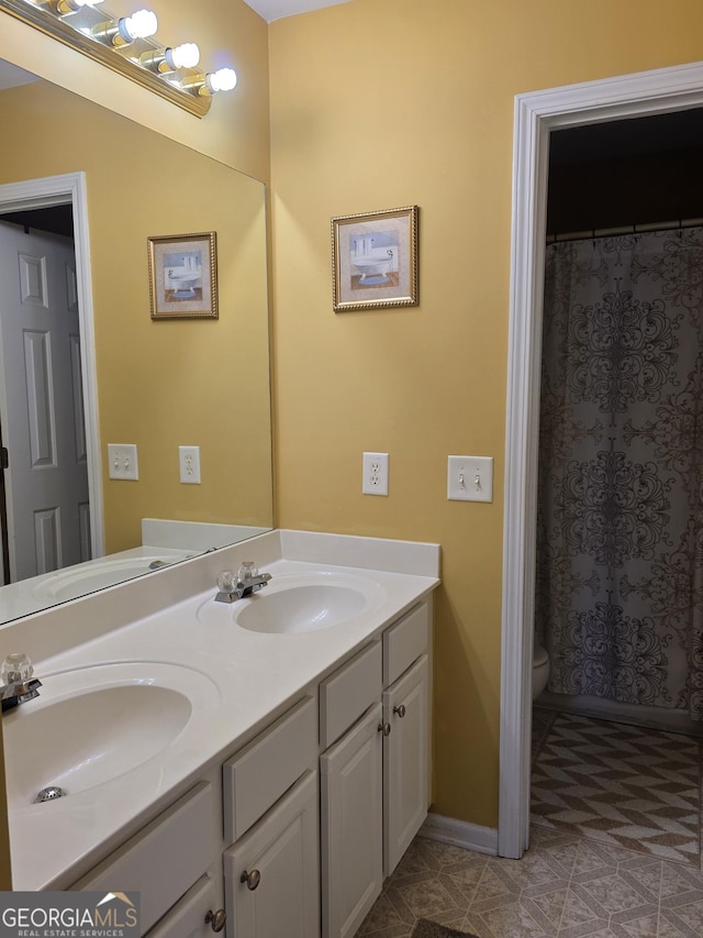 bathroom with baseboards, a sink, toilet, and double vanity