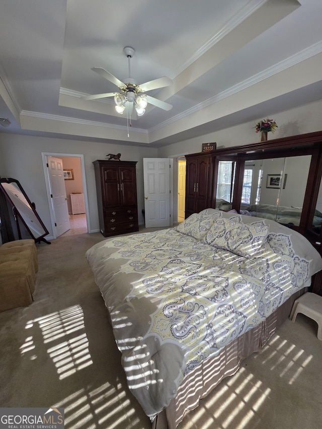 carpeted bedroom with a tray ceiling, crown molding, and ceiling fan