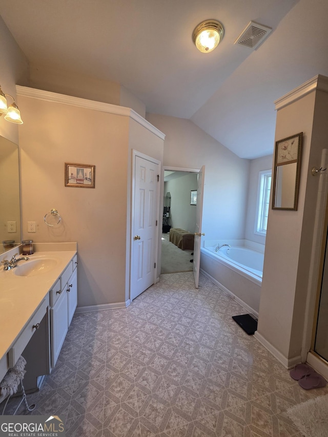 ensuite bathroom featuring baseboards, visible vents, a garden tub, vaulted ceiling, and vanity