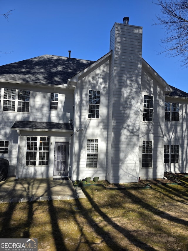 view of front facade with a patio, a chimney, and roof with shingles