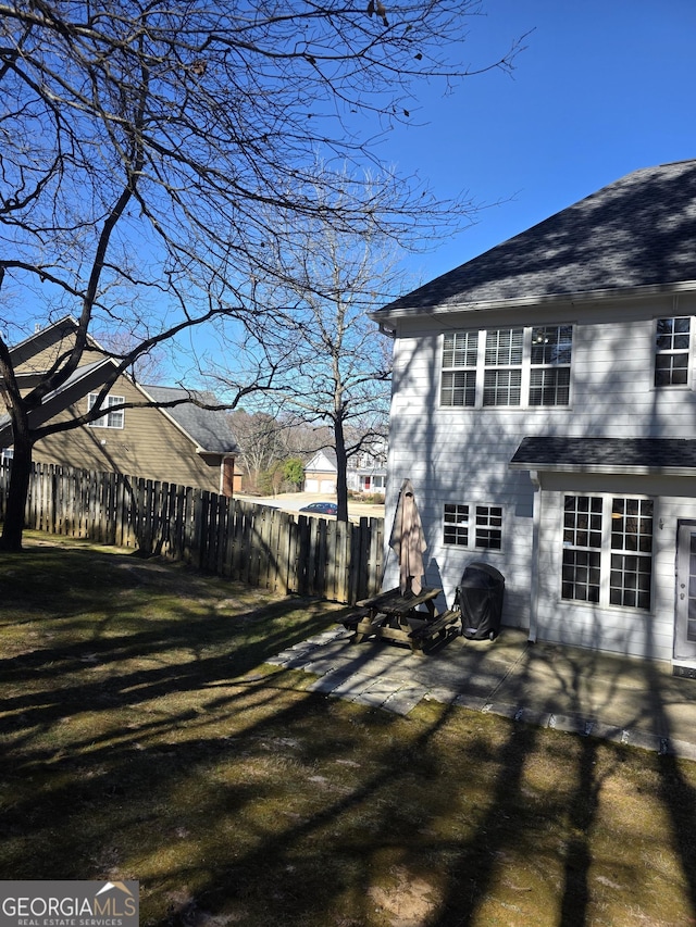 view of side of home with a shingled roof, a patio area, fence, and a lawn