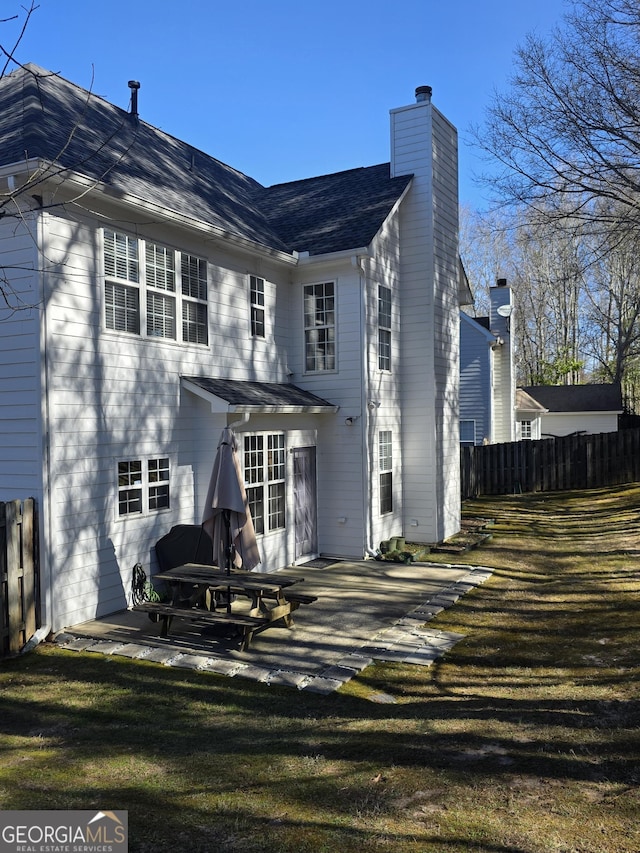 rear view of house with a patio, a chimney, fence, and a lawn