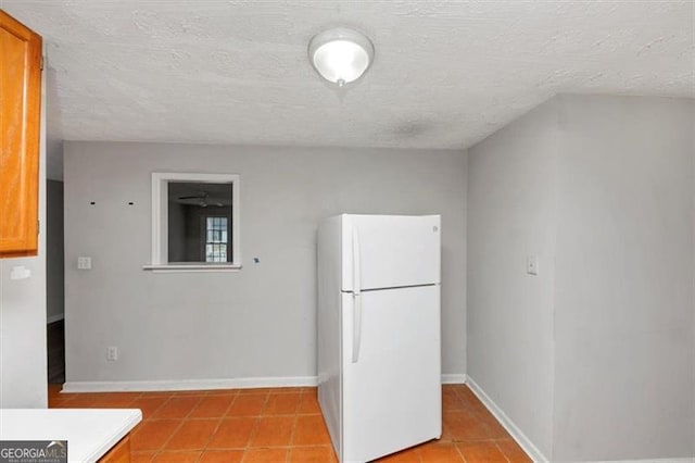 kitchen featuring brown cabinetry, freestanding refrigerator, light tile patterned flooring, a textured ceiling, and baseboards