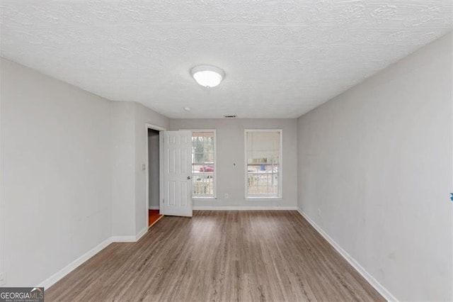 empty room featuring a textured ceiling, baseboards, and wood finished floors