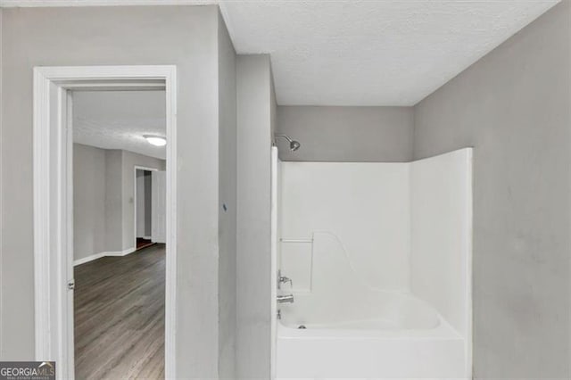 full bath featuring a textured ceiling, shower / bath combination, wood finished floors, and baseboards