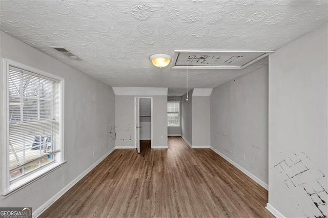 interior space featuring a textured ceiling, wood finished floors, visible vents, baseboards, and attic access