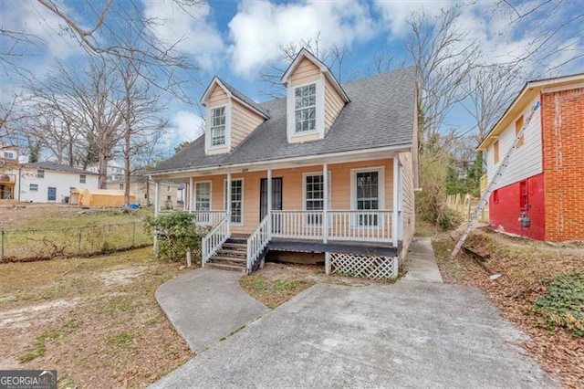 cape cod home featuring covered porch, a shingled roof, and fence