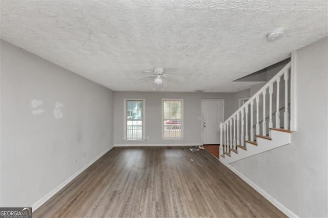 unfurnished living room featuring wood finished floors, a textured ceiling, baseboards, and stairs