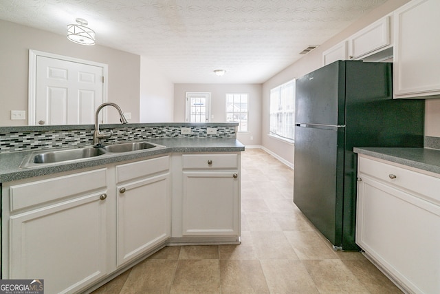 kitchen with visible vents, dark countertops, freestanding refrigerator, a sink, and backsplash