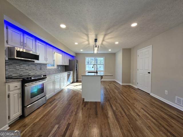 kitchen featuring tasteful backsplash, dark wood finished floors, a kitchen island with sink, stainless steel appliances, and a sink