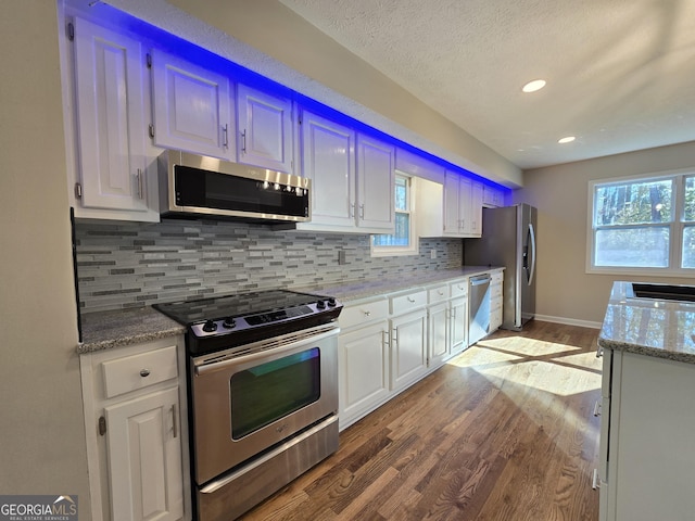 kitchen featuring backsplash, white cabinetry, stainless steel appliances, and wood finished floors