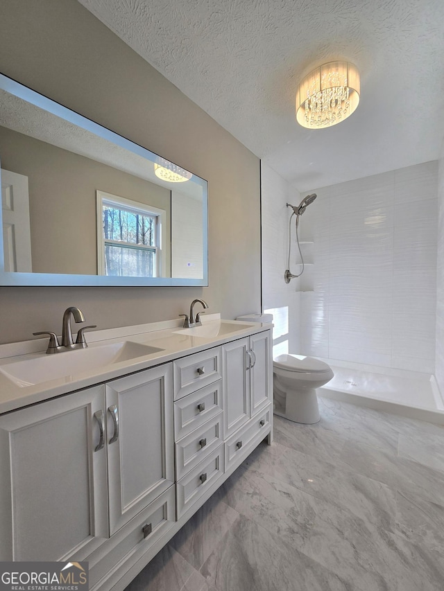 bathroom with marble finish floor, tiled shower, a sink, and toilet