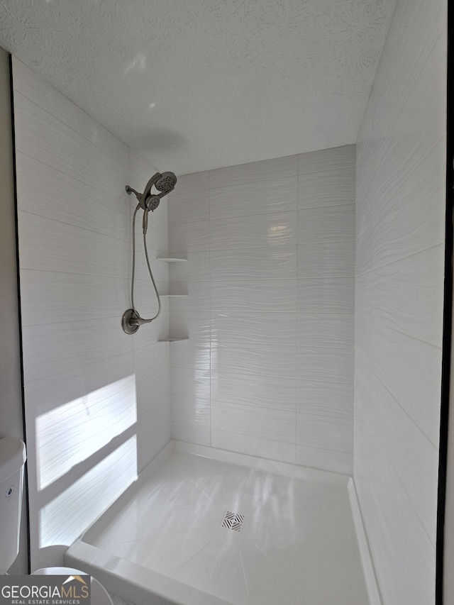 full bath featuring a textured ceiling, tiled shower, and toilet