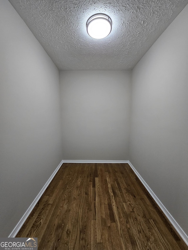 unfurnished room featuring a textured ceiling, dark wood finished floors, and baseboards