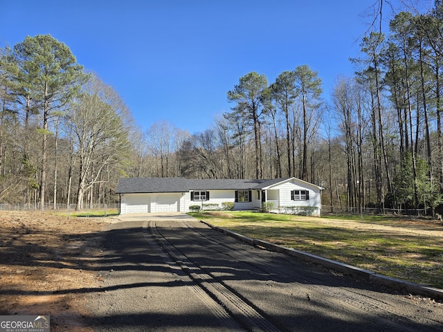 view of front of home with a front yard, fence, a view of trees, a garage, and driveway