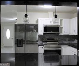 kitchen with stainless steel appliances, dark countertops, white cabinets, and backsplash