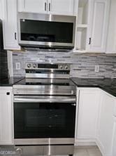 kitchen featuring stainless steel appliances, dark countertops, white cabinets, and decorative backsplash