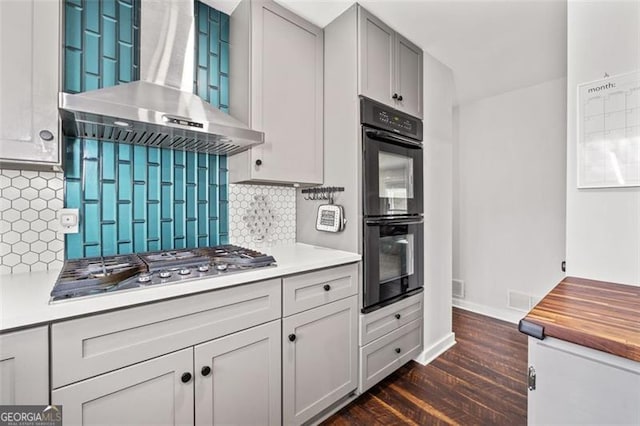 kitchen featuring dobule oven black, stainless steel gas stovetop, decorative backsplash, dark wood-type flooring, and wall chimney exhaust hood